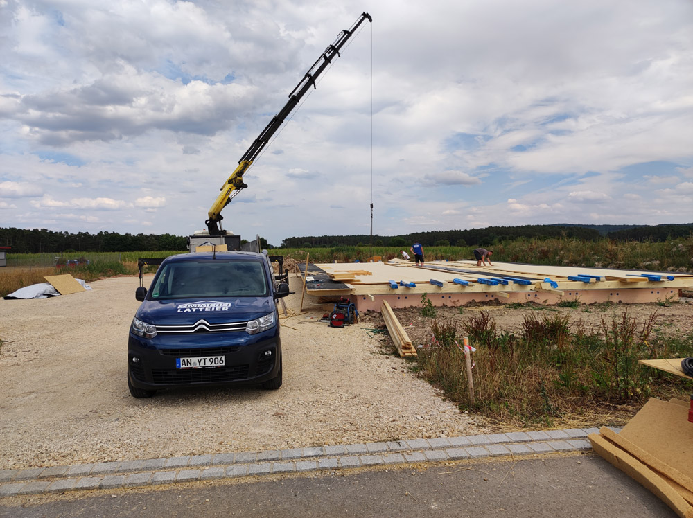 Firmenauto vor dem Autokran beim Aufrichten der Holzwände
